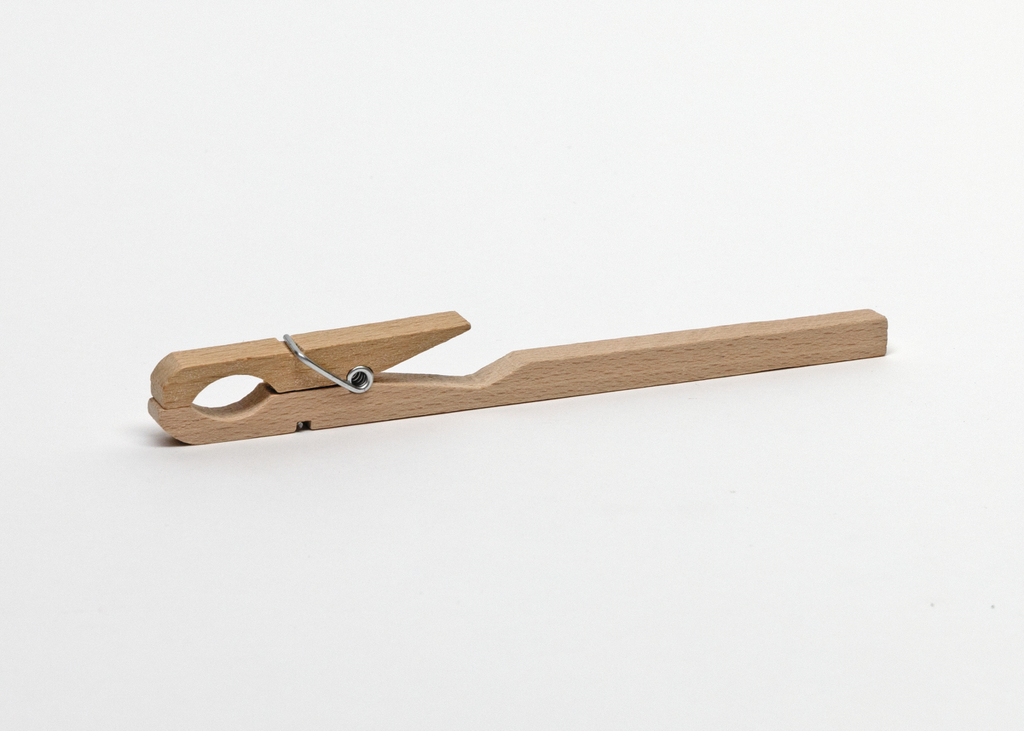 Das Bild zeigt eine Holzklammer, die in der Mitte einen metallischen Federmechanismus aufweist. Dieses einfache Hilfsmittel wird oft in Experimenten verwendet, um Objekte zusammenzuhalten oder an etwas zu befestigen.