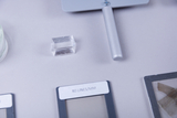 Das Bild zeigt verschiedene Experimentiermaterialien, darunter ein klarer Kristall, ein Werkzeug mit einem langen Griff und mehrere Platten mit Beschriftungen. Diese Objekte scheinen für wissenschaftliche oder schulische Experimente im Bildungswesen gedacht zu sein.