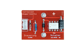 Das Bild zeigt eine rote Platine, die Teil eines Experimentierkits ist, mit verschiedenen elektronischen Komponenten wie Widerständen und einem Schalter. Beschriftungen auf der Platine weisen auf die Funktionalitäten und Spannungswerte der Bauteile hin.