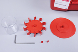 Das Bild zeigt verschiedene Teile eines Experimentier-Sets für den Physikunterricht, darunter einen durchsichtigen Becher, ein rotes Zahnradsystem sowie eine runde Plattform und einige Verbindungselemente. Diese Komponenten sind für praktische physikalische Experimente konzipiert.