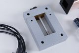 Das Bild zeigt ein metallisches, graues Experimentiergerät mit einer geschlitzten Öffnung und einer Stange in der Mitte. Daneben sind mehrere elektrische Kabel und andere Bauteile zu sehen, die für experimentelle Zwecke verwendet werden können.