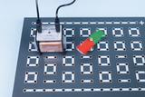Das Bild zeigt ein Experimentierfeld mit einem Elektromotor und einem drehenden rot-grünen Propeller. Der Motor ist an einem Blech montiert, das mit verschiedenen Anschlusslöchern für elektrische Verbindungen ausgestattet ist.