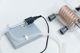 Das Bild zeigt eine experimentelle Apparatur, bestehend aus einer grauen Basis mit einem Anschluss und einem Kupferrohr in einer transparenten Kammer. Diese Geräte könnten verwendet werden, um chemische Reaktionen oder physikalische Prozesse im Bildungsbereich zu demonstrieren.