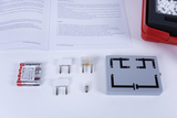 Das Bild zeigt verschiedene Bauteile für Experimente im Bereich Elektronik—darunter Batterien, Glühlampen und ein Modell zur Schaltkreisbildung. Neben den Komponenten liegt ein Arbeitsblatt mit Fragen zur Erklärung der Experimente auf.