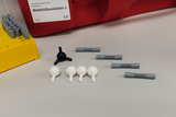 Das Bild zeigt einen Molekülbaukasten bestehend aus bunten Kunststoffteilchen, darunter schwarze und weiße Kugeln sowie graue Verbindungsstücke. Daneben befindet sich ein gelber Halter für die Teile, und im Hintergrund steht eine rote Box mit dem Label „Molekülbaukästen 1“.