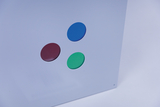 Das Bild zeigt eine flache Oberfläche in hellem Blau mit drei farbigen runden Plättchen: rot, grün und blau. Diese Plättchen scheinen als Teil eines Experimentiermaterials für Unterrichtszwecke konzipiert zu sein.
