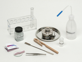 Das Bild zeigt eine Auswahl an Laborgeräten und Chemikalien, darunter ein Reagenzglashalter, ein Brenner, Demineralisiertes Wasser, Raschigranulat und verschiedene Werkzeuge. Diese Ausstattung ist ideal für schulische Experimente im naturwissenschaftlichen Unterricht.
