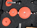 Das Bild zeigt ein Set von roten Rollen und Elementen, die in einem Schaumstoffpolster angeordnet sind. Diese Teile gehören vermutlich zu einem Experimentiersystem, das für Bildungszwecke im MINT-Bereich eingesetzt wird.