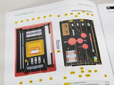 Das Bild zeigt eine übersichtliche Darstellung eines Schüler-Sets für mechanische Experimente, das verschiedene Bauteile in einem roten Kasten enthält. Jedes Teil ist nummeriert und annotated, um die Nutzung im Bildungsbereich zu erleichtern.