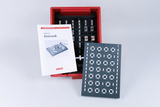 Das Bild zeigt ein Elektronik-Experimentier-Set von Cornelsen in einer roten Box. Neben der Box liegt das Handbuch mit Anleitungen, während eine Leiterplatte mit verschiedenen Kontakten für Experimente sichtbar ist.
