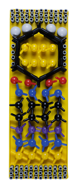 Das Bild zeigt ein Modellbau-Set zur Darstellung von Molekülen, bestehend aus verschiedenen farbigen Kugeln und Stangen, die atomare Strukturen symbolisieren. Das Set befindet sich auf einer gelben Basis und dient zur Förderung von naturwissenschaftlichem Lernen im Bildungsbereich.