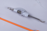 Das Bild zeigt ein Experimentiergerät mit einem grauen Kunststoffelement und einem metallischen, gebogenen Draht. Darüber hinaus liegt ein orangefarbenes, stabförmiges Objekt daneben, das ebenfalls für experimentelle Zwecke verwendet werden könnte.