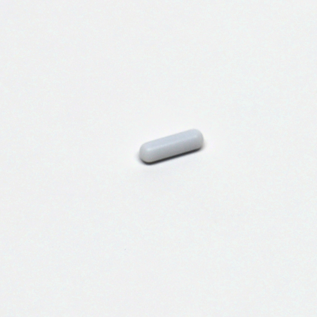 Das Bild zeigt eine kleine, weiße, längliche Pille oder Tablette, die auf einem weißen Hintergrund liegt. Sie scheint ein Experimentiermaterial zu sein, das möglicherweise in wissenschaftlichen oder educational Kontexten verwendet wird.