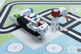 Das Bild zeigt eine Konstruktion aus modularen Bauelementen, die als Roboterarm dient und auf einer farbigen Unterlage positioniert ist. Diese Kombination aus Technik und Anleitung ist ideal für Experimente im Bildungsbereich.