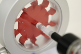 Das Bild zeigt ein rot gefärbtes Experimentiergerät, das mit einer transparenten Spritze verbunden ist. Es dient wahrscheinlich zur Durchführung von physikalischen Experimenten im Bildungswesen, um verschiedene Konzepte zu verdeutlichen.
