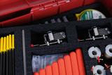 Das Bild zeigt eine rote Box, die verschiedene Experimentiermaterialien enthält, darunter gelbe und rote Stäbe sowie mechanische Komponenten. Die Materialien sind in Schaumstoffpolsterungen angeordnet, um einen sicheren Transport und eine ordentliches Aufbewahrung zu gewährleisten.