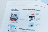 Das Bild zeigt Materialien für den Unterricht mit dem eXperiBot Lernroboter, zusammengestellt in einer roten Box. Es werden verschiedene Unterrichtsmaterialien wie „Smarte Fabrik“ und „Labyrinth“ aufgeführt, die parallel zu den Robotern eingesetzt werden können.
