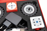 Das Bild zeigt einen Kasten mit verschiedenen Experimentierkomponenten, darunter elektronische Module, Räder und ein Netzteil. Diese Teile sind für den Bildungsbereich konzipiert, um Schülern praktisches Lernen und Experimentieren zu ermöglichen.