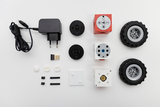 Das Bild zeigt eine Anordnung verschiedener Komponenten eines Experimentierkits, darunter ein Ladegerät, USB-Stick, elektronische Bausteine und Räder. Die Teile sind darauf ausgelegt, um Schülern das Programmieren und den Bau von Robotern zu ermöglichen.