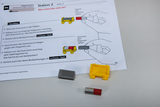 Das Bild zeigt Materialien für einen Experimentierauftrag zum Thema Magnetismus, einschließlich einer Anleitung auf einem Arbeitsblatt. Zu sehen sind ein Gelbewagen, verschiedene Eisenstücke und ein Magnet, die für praktische Experimente genutzt werden sollen.
