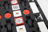 Das Bild zeigt ein Set von Bausteinen und Komponenten, die in einer gepolsterten Schaumstoffeinlage angeordnet sind. Die Teile umfassen verschiedene mechanische und elektrische Elemente, die für experimentelle Lernprojekte im Bildungsbereich genutzt werden können.