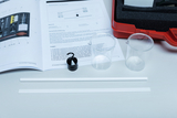 Auf dem Tisch liegen ein Lehrbuch und verschiedene Materialien für Experimente, darunter zwei transparente Becher und zwei weiße Kunststoffstreifen. Anhand der beiliegenden Anleitung können Schüler physikalische Phänomene untersuchen und beobachten.