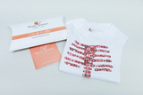 Eine weiße T-Shirt mit einer bunten Darstellung eines Skeletts ist auf einem Tisch liegend abgebildet. Daneben befindet sich eine stilvolle Verpackung mit dem Aufdruck "Body Planet - A FUN WAY TO LEARN!", die den edukativen Ansatz des Produkts betont.