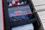 Im Kasten sind mehrere transparente Behälter mit unterschiedlich farbigen Spielmarken und Würfeln sowie kleine quadratische Blöcke aus Material, das wie Schaumstoff aussieht. Diese Materialien sind für Experimentier- und Lernzwecke im Bildungswesen geeignet.