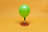 Eine grüne Luftballon steht auf einer roten Basis. Er ist mit einem Verbindungselement ausgestattet, das die Demonstration von physikalischen Prinzipien ermöglichen könnte.