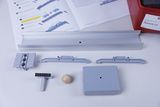 Auf dem Tisch liegen verschiedene graue Komponenten, die wahrscheinlich zu einem Experimentierset gehören, sowie eine Anleitung. Ein hölzerner Ball und ein kleines Werkzeug sind ebenfalls zu sehen, was auf eine physikalische Demonstration hinweist.