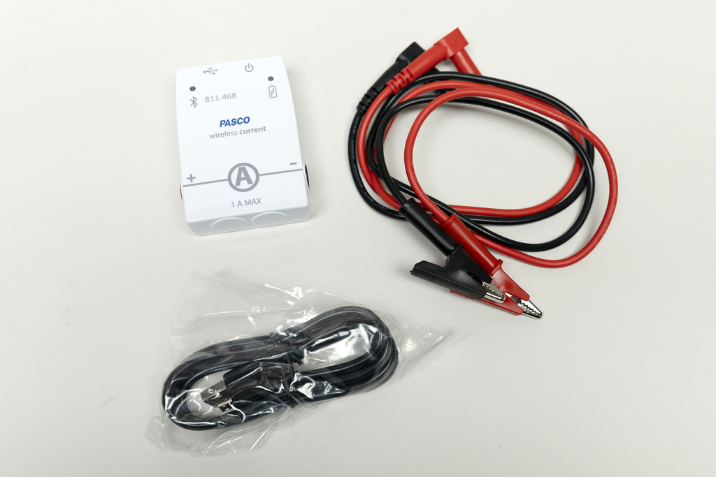 Zu sehen sind ein drahtloses Messgerät zur Erfassung von elektrischem Strom und zwei Sicherheitsmessleitungen in Rot und Schwarz. Zusätzlich liegt ein Kabel in einer Plastikhülle bei, das vermutlich für die Verbindung oder Stromversorgung dient.