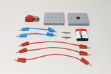 Ein Set für Elektrizitätsexperimente enthält eine Batterie, einen Klingelton, Schalter und Verbindungskabel. Ergänzt wird der Aufbau durch rote und blaue Leitungen sowie zwei Krokodilklemmen.