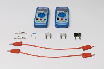 Zwei blaue Digitalmultimeter von PeakTech liegen über verschiedenen elektronischen Bauteilen wie Widerständen, Sicherungen und Klemmen. Im Vordergrund befinden sich zwei rote Verbindungskabel mit Steckern.
