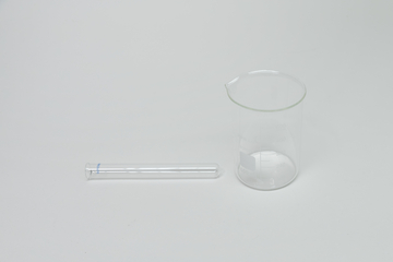 Ein durchsichtiges Becherglas aus Glas steht auf einer weißen Oberfläche. Daneben liegt ein passender Glasdeckel.