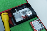 Ein Set aus physikalischen Experimentierutensilien liegt in einer roten Kunststoffbox. Zu sehen sind eine gelbe Taschenlampe, Batterien, diverse Metallteile und eine kleine weiße Box.