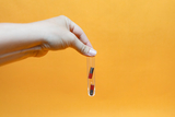 Eine Hand hält ein schmales Reagenzglas vor einem gelben Hintergrund. Im Inneren des Glases befinden sich zwei kleine, rot-schwarze Magnete.