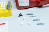 Ein Molekülbaukasten für den Chemieunterricht ist mit gelben Halterungen und einer roten Box abgebildet. Einzelne graue Verbindungsstücke sowie weiße und schwarze Atome liegen lose auf der hellen Oberfläche.