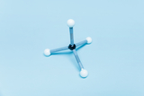 Ein molekulares Modell zeigt ein zentrales schwarzes Atom, das mit drei weißen Atomen verbunden ist. Die Anordnung stellt eine tetraedrische Struktur vor einem hellblauen Hintergrund dar.