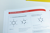 Ein Lehrbuch zeigt chemische Strukturformeln von Benzol und Cyclohexan. Neben den Zeichnungen befinden sich erklärende Texte zu aromatischen Kohlenwasserstoffen und entsprechenden Molekülbaukästen.