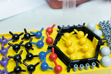 Ein gelbes Modellbau-Set zeigt verschiedene Molekülbaukästen mit farbigen Kunststoffkugeln und Verbindungsstücken. Die Elemente sind in einer Kunststoffbox angeordnet und dienen der Veranschaulichung chemischer Strukturen.