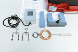 Ein Physik-Experimentierset zur Demonstration elektromagnetischer Prinzipien liegt auf einem weißen Tisch. Es umfasst einen Transformator, Hufeisen- und Stabmagnete sowie Kupferspulen und Zubehör.