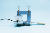 Ein elektrischer Induktionserhitzer mit Steuereinheit steht auf einer blauen Halterung. Ein Metallstab mit Holzgriff liegt in der kupferfarbenen Induktionsspule.