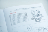Ein offenes Lehrbuch zum Thema Brandschutzerziehung zeigt einen Textabschnitt über den Umweltbezug. Eine begleitende Illustration stellt eine Szene mit Kindern und einem Teddybären dar.