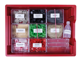 Ein rotes Sortimentskästchen enthält verschiedene Materialien wie Pappe, Stahlwolle, Holzstäbchen und Kunststoffe für Experimente. Ergänzt wird das Set durch Baumwollstoff sowie eine Flasche Tafelessig.