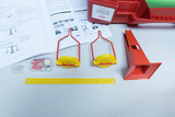 Ein Set zum Thema Waagen und Gleichgewicht besteht aus einer roten Waage, gelben Schalen und einem Lineal. Ergänzt wird das Experimentierkit durch eine Anleitung sowie eine Box mit verschiedenen Kleinteilen.